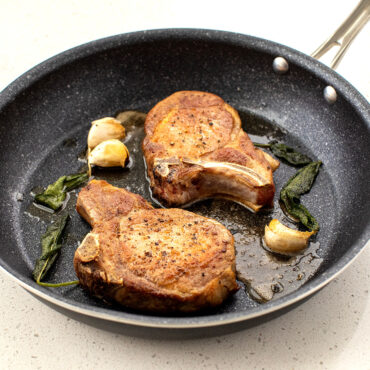 An image of a black 12-in saute skillet with a white speckled pattern with cooked pork chops in the pan ready to be plated.