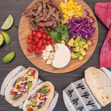 Grilled fajita scene with two taco racks filled with grilled tortillas and filled with toppings.