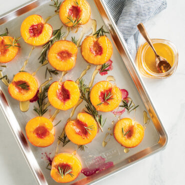 overhead image of peaches halved on the baker's half sheet with olive oil and rosemary.