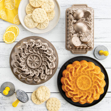 Group shot of Citrus Bakeware Collection including Citrus Twist Cake Pan, Citrus Blossom Loaf and Citrus Cookie Stamps. Includes citrus cake on platter and cookies with product.