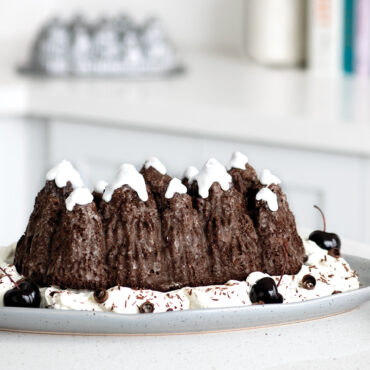 The image features a mouthwatering chocolate cherry loaf cake with fluffy white icing resembling snow-covered pine trees. placed on the kitchen counter.