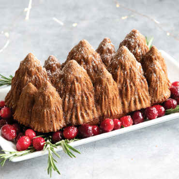Alpine Forest Loaf Pan - A beautifully designed loaf pan featuring an enchanting alpine forest motif. The intricate details of the trees, mountains, and wildlife create a captivating scene, placed on top of cranberries for a holiday scene, making it a perfect addition to your baking collection.
