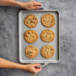 ProCast Half Sheet - A versatile and reliable half sheet pan designed for professional and home bakers. in this image you can see hands picking up sheet pan filled with chocolate chip cookies.
