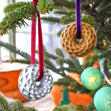 Two Nordic Ware collectible cast metal Jubilee Bundt ornaments in gold and silver finishes hanging on Christmas tree