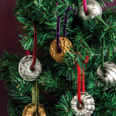 Two Nordic Ware collectible cast metal Jubilee Bundt ornaments in gold and silver finishes hanging on Christmas tree