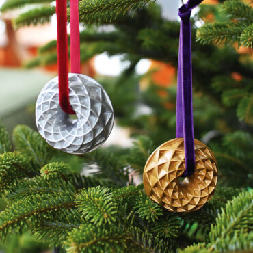 Two Jubilee Bundt ornaments in gold and silver hanging on a Christmas tree.