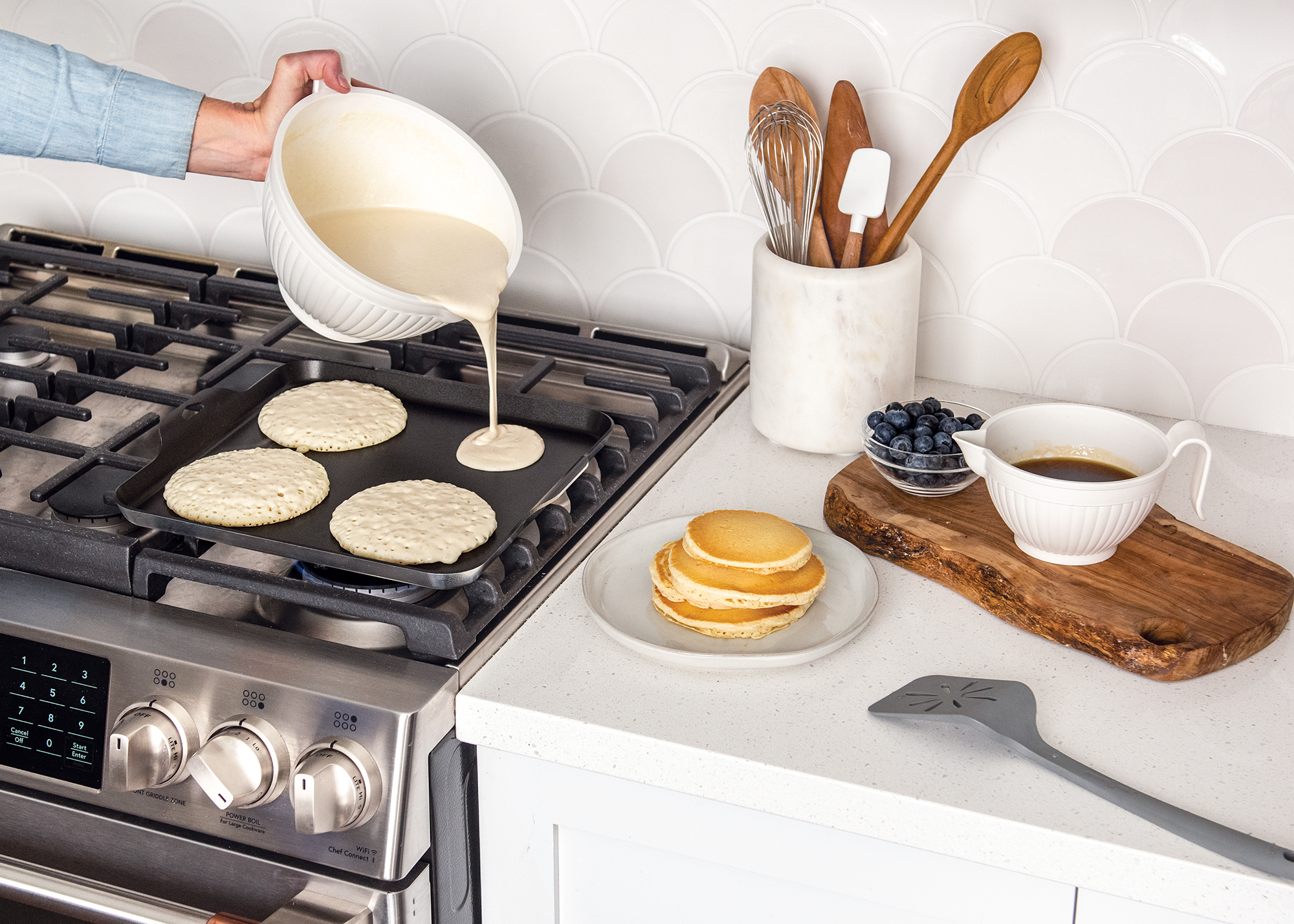 Hand pour pancake batter on square griddle on stovetop in breakfast scene