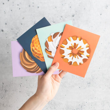 Hand holding 4 colored Bundt greetings cards in a fan-like shape