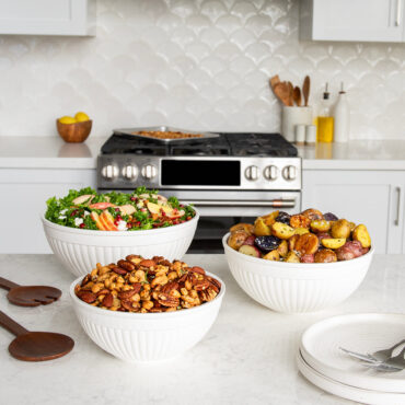 Nordic Ware 3 piece white prep and serve 5 quart, 3.5 quart and 2 quart bowls on kitchen countertop filled with salad, potatoes, and mixed nuts