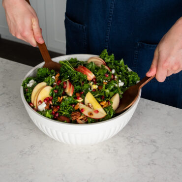 hands using utensils in nordic ware white 5 quart bowl filled with salad