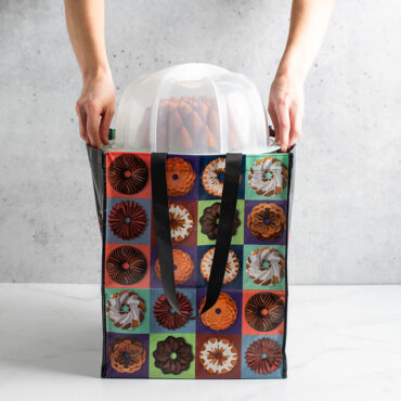 Hands placing Nordic Ware Bundt Keeper with a cake inside of large Bundt Tote Bag