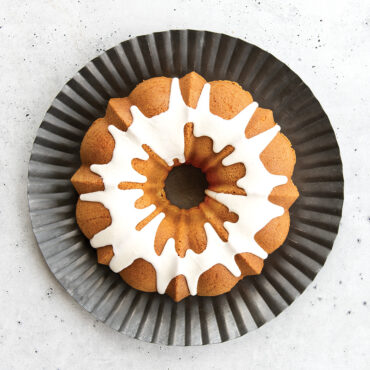 Golden vanilla bundt cake with white glaze drizzled on top, served on white plate