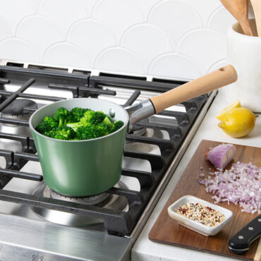 Nordic Ware cardamom ceramic nonstick 1.5 quart saucepan with lid, containing steamed green broccoli on stovetop