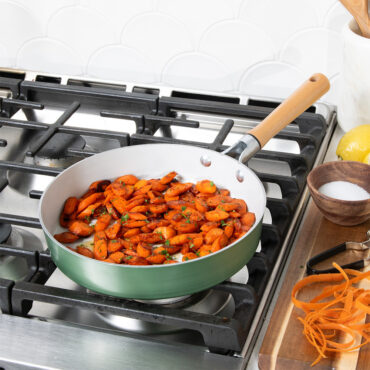 Nordic Ware cardamom ceramic nonstick 10-inch skillet on stovetop with diced carrots cooking inside