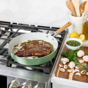 Nordic Ware cardamom ceramic nonstick 12-inch skillet on stovetop with seared steak, ingredients on cutting board