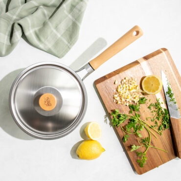 Nordic Ware Cardamom 3-quart aluminum saucepan with lid, overhead view with fresh lemons and herbs on wooden cutting board