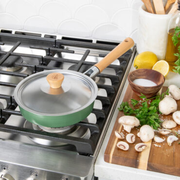 Nordic Ware Cardamom 8-inch nonstick frying pan with glass lid on stovetop, cream-colored exterior finish