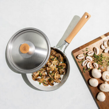 Nordic Ware Cardamom 8-inch nonstick saute pan with glass lid, cooked golden mushrooms inside, raw mushrooms nearby