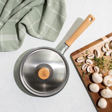 Nordic Ware Cardamom 8-inch nonstick saute pan with lid, cream colored exterior, raw sliced mushrooms nearby