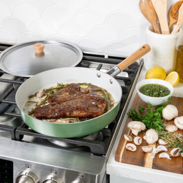 Nordic Ware Cardamom 12-inch nonstick frying pan with glass lid containing seared steak, golden aluminum finish