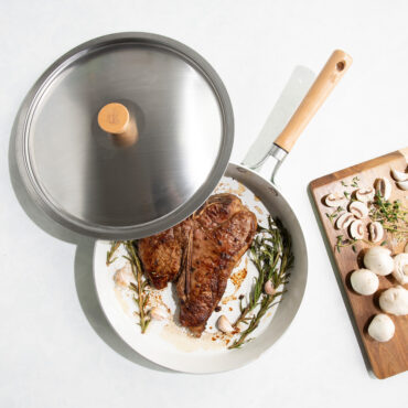 Nordic Ware Cardamom 12-inch nonstick frying pan with glass lid, containing seared steak, overhead view