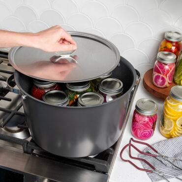 16qt Stock Pot with Lid on stovetop filled with jars; hand placing lid onto stock pot