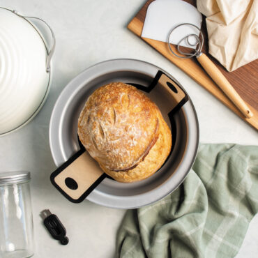 Overhead image of baked sourdough bread in Nordic Ware's bread baking pan with tools and accessories around it.