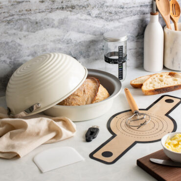 Image of Nordic Ware's Deluxe Sourdough Baking Kit with baked sourdough bread in bread baking pan and baking tools in kit around it in kitchen scene