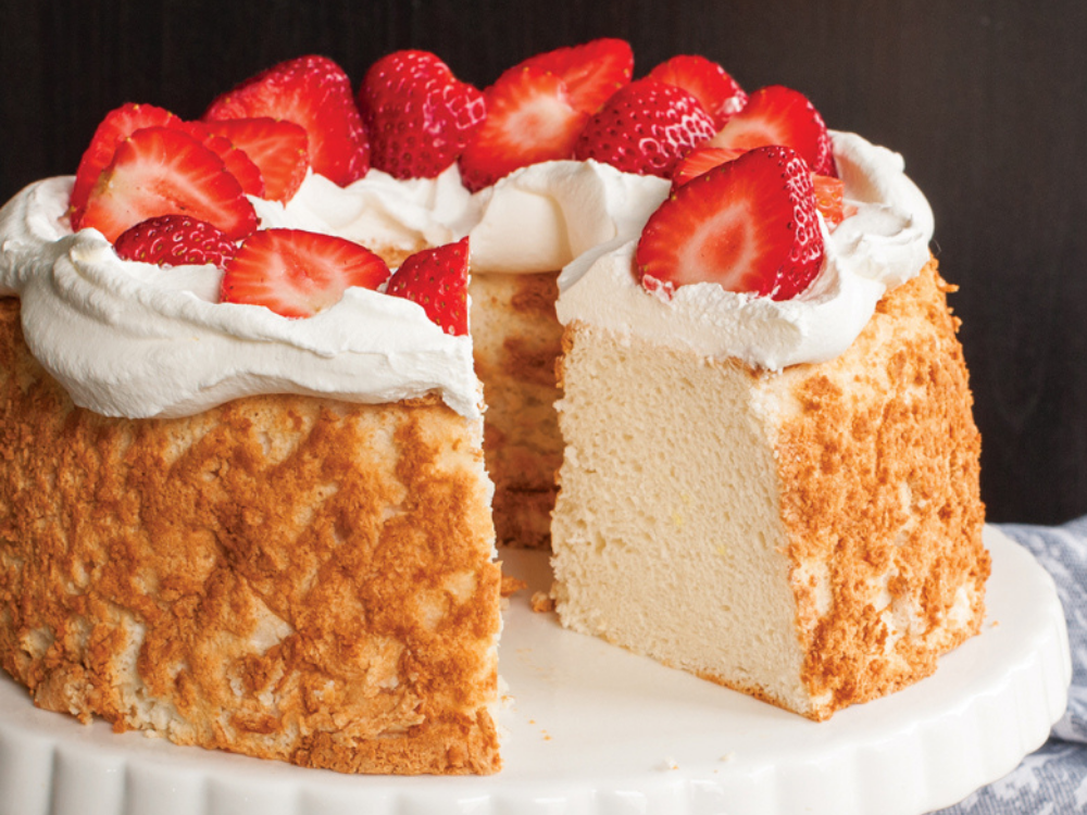 Angel food cake topped with whipped cream and strawberries with a slice removed 