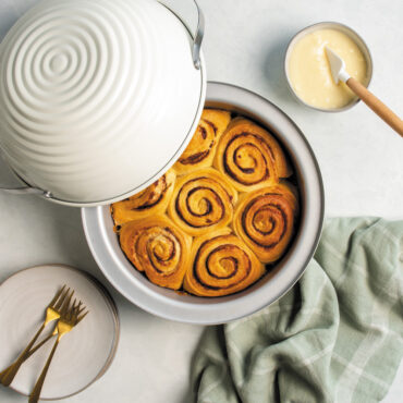 Overhead image of baked sourdough cinnamon rolls with glaze in a bowl on the side