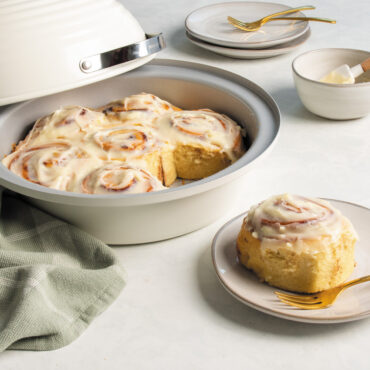 Angled image of baked cinnamon rolls in Nordic Ware's Bread Baking Pan with one roll in a plate