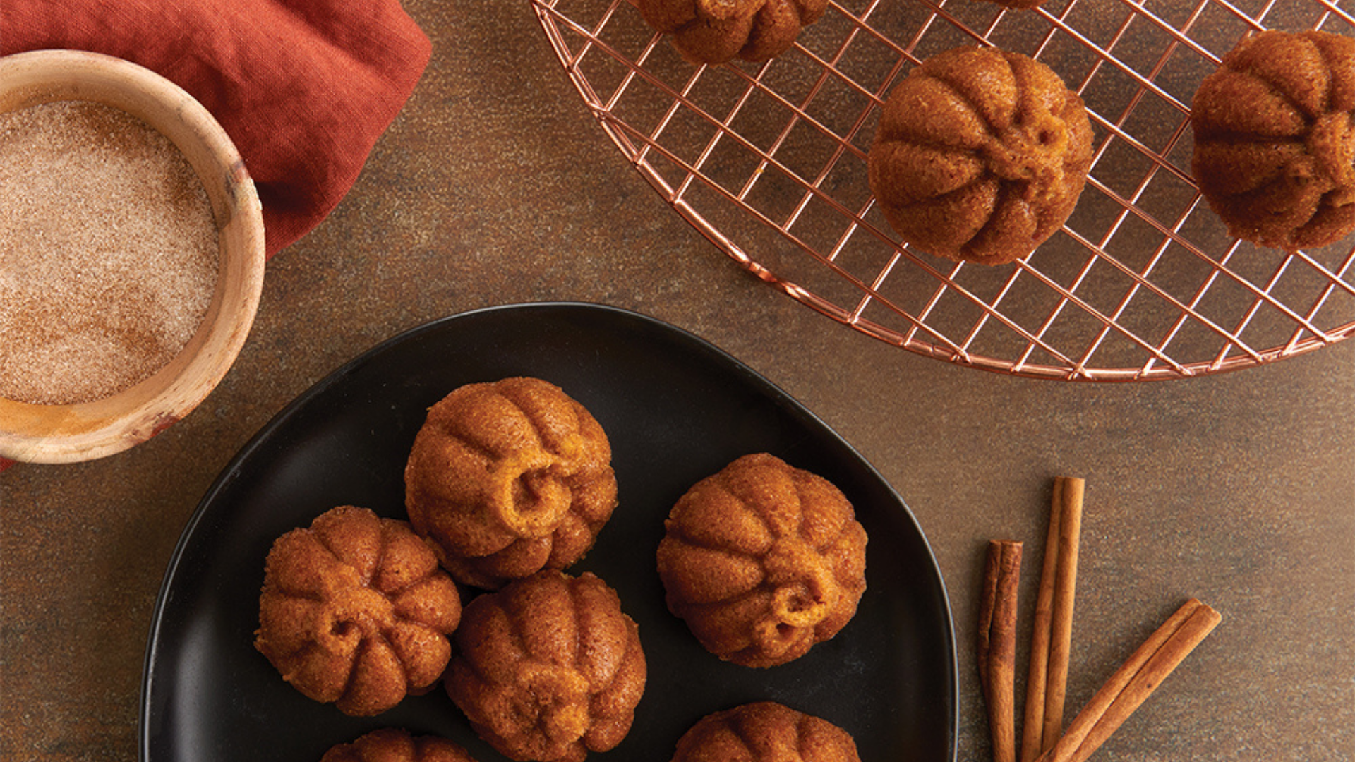Lil's Pumpkin Cakelets cooling on a wire rack next to a plate of cooled cakelets.