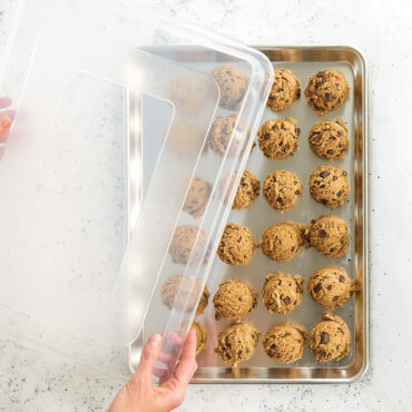 Half Sheet with cookie dough balls and hands placing a lid on top