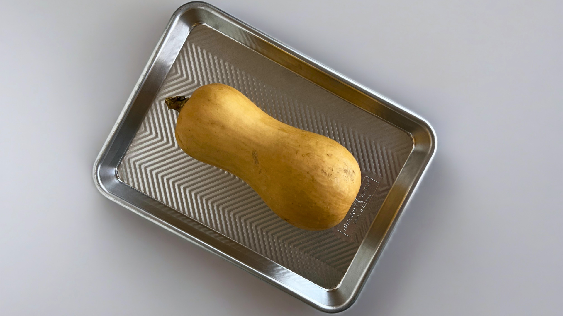 A whole butternut squash on a Prism Quarter Sheet Pan ready to be roasted. 
