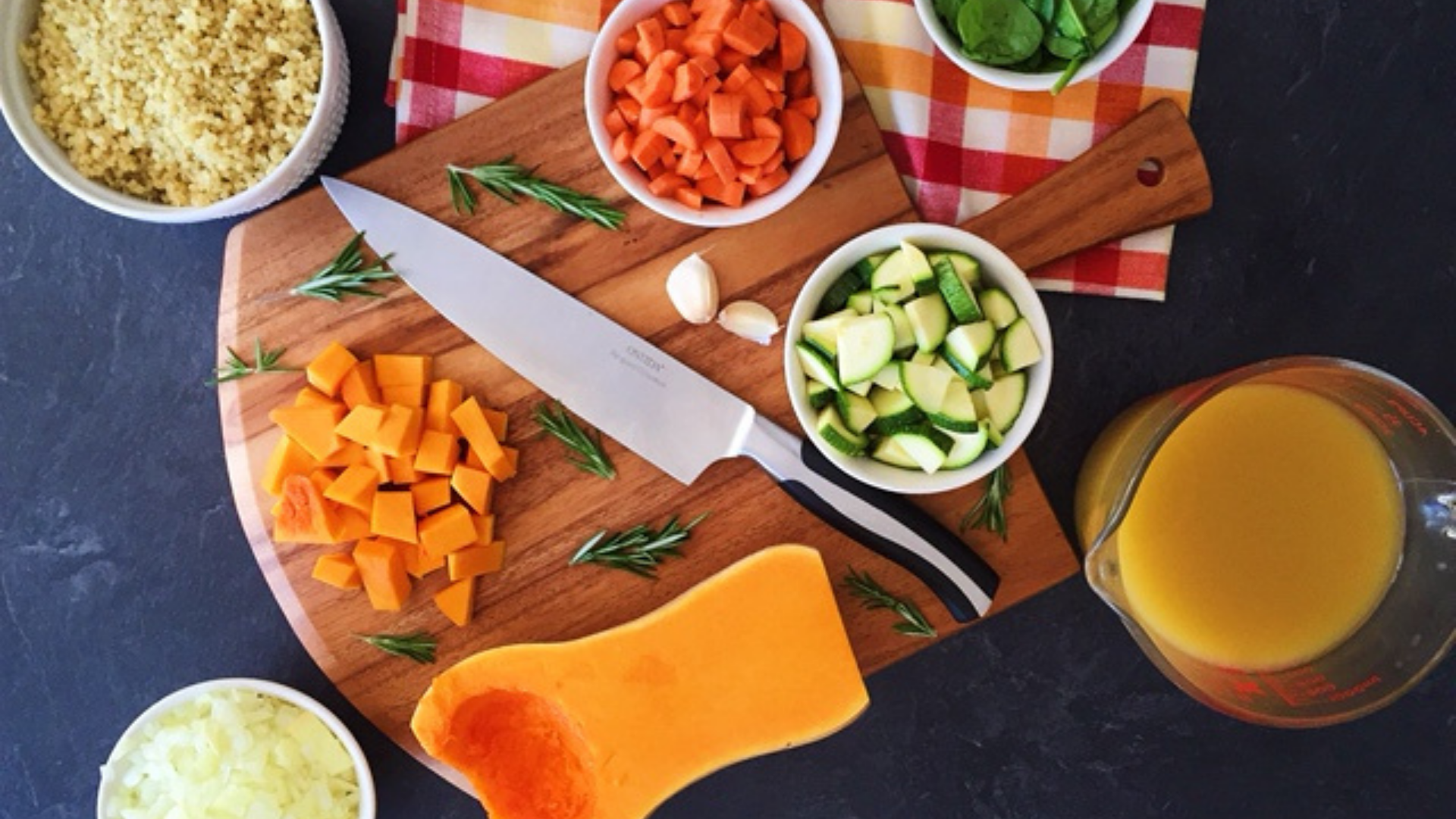 Butternut squash being chopped on a cutting board with ingredients to make butternut squash soup on the side. 