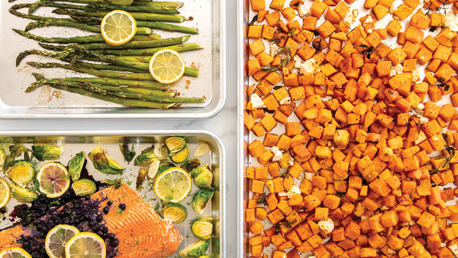 Three sheet pans: one with roasted butternut squash, one with roasted asparagus with lemon, and one with roasted salmon with brussels sprouts. 