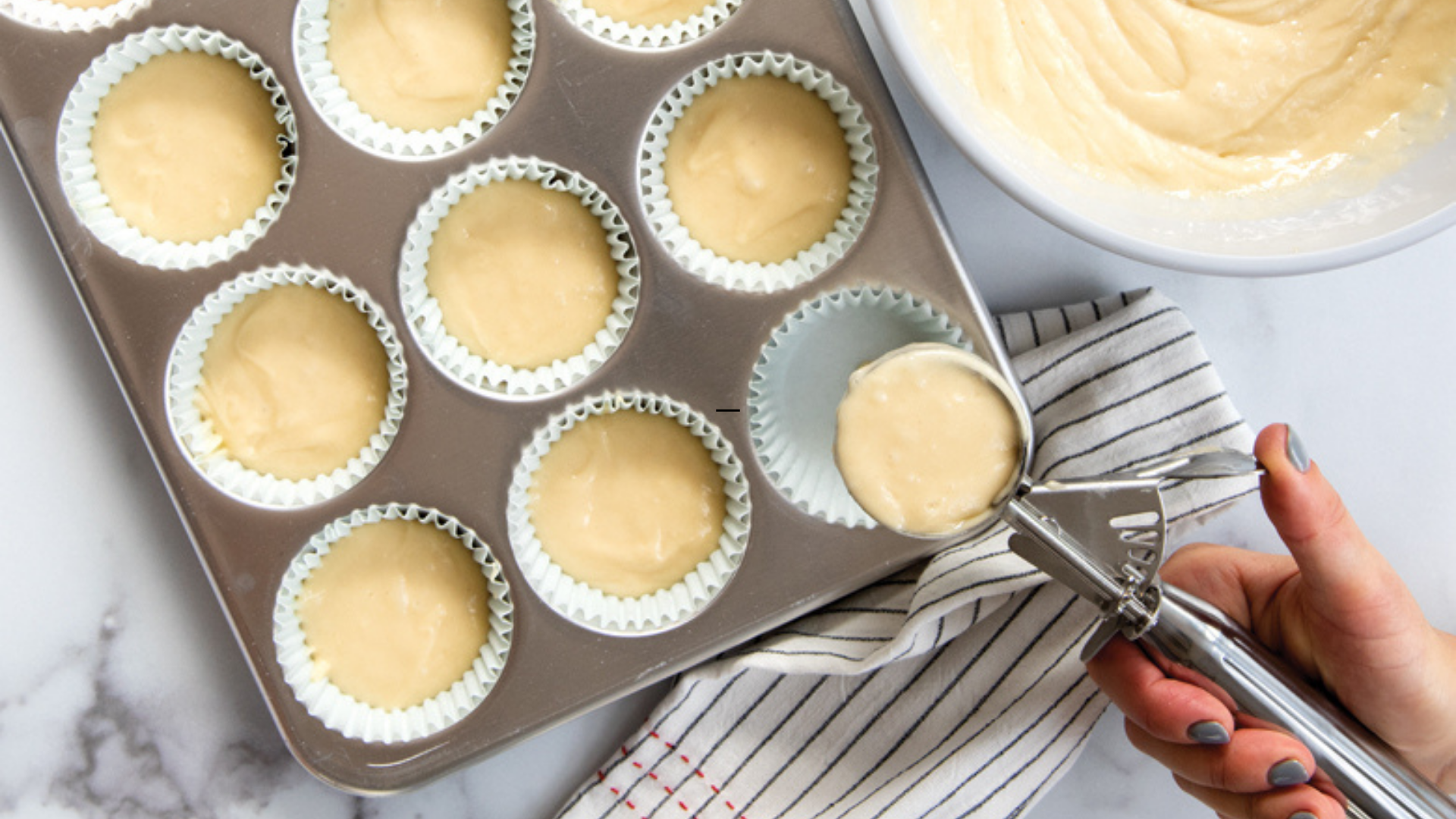 12-cavity Naturals® Muffins pan being filled with batter using a cookie scoop.