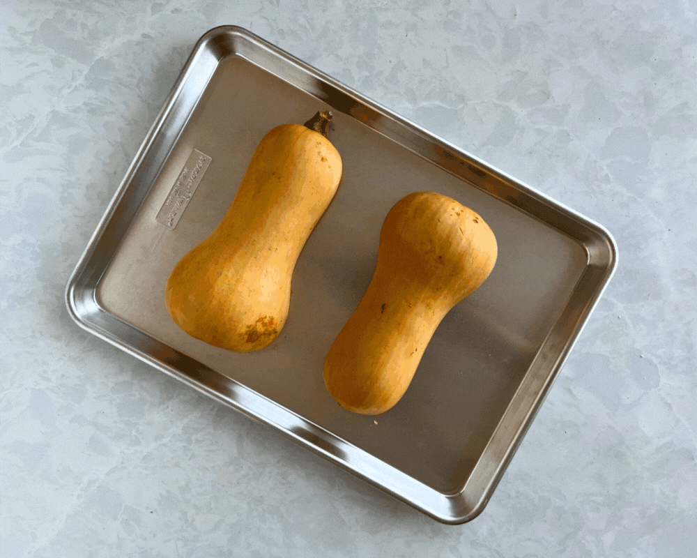 Two halves of a butternut squash on a baking sheet ready to be roasted. 