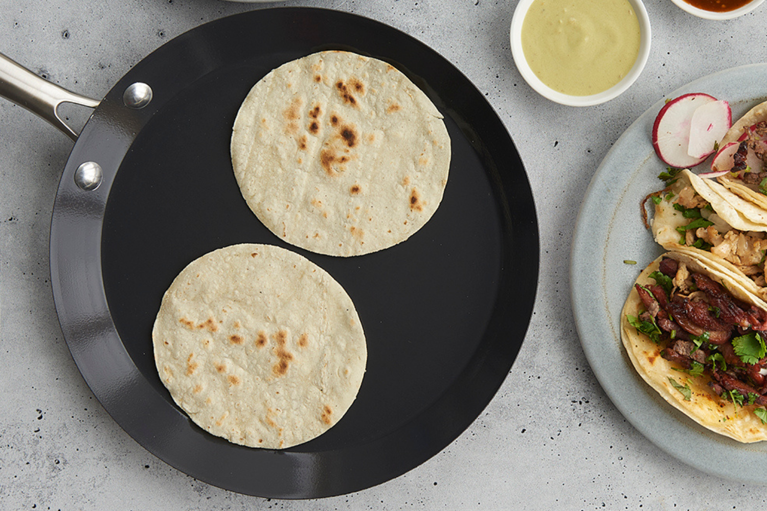 Traditional French Steel Crepe Pan with tortillas warming in it next to a plate of assembled tacos.