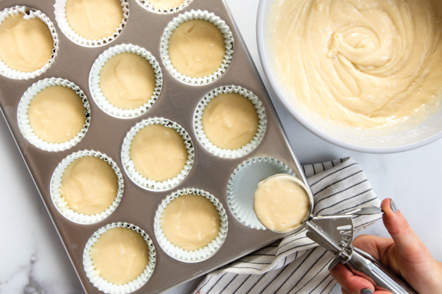 Filling a Naturals® 12 Cavity Muffin Pan with Batter Filling a Naturals® 12 Cavity Muffin Pan with muffin batter using a cookie scoop.