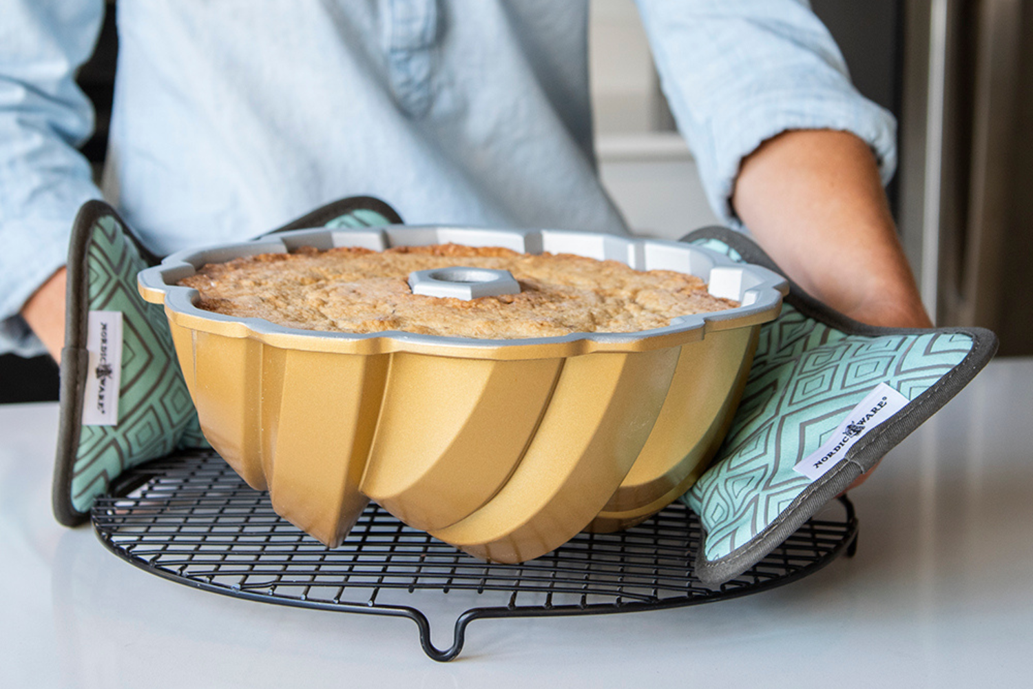 Bundt® Hot Pad Set of 2 75th Anniversary Braided Bundt® Pan being placed on a wire cooling grid with Bundt® Hot Pad Set of 2.