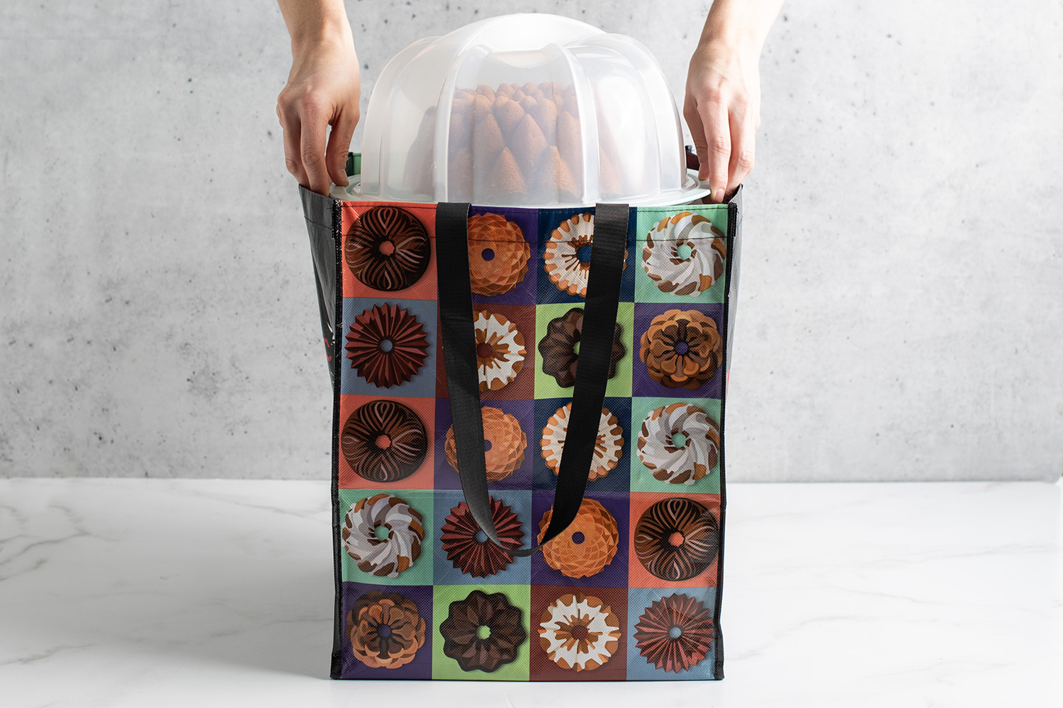 Hands removing a Bundt cake and keeper from a Bundt tote bag. 