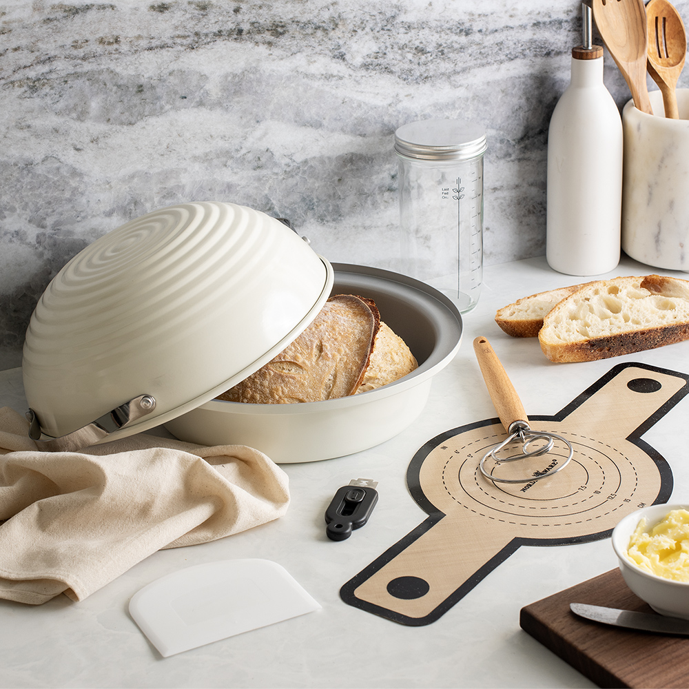 Image of sourdough baking kit tools in a kitchen scene with a baked sourdough loaf of bread