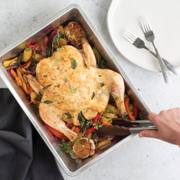 Roasted Turkey inside pan, hand using tongs to grab veggies