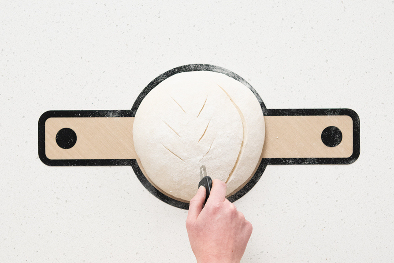 Scoring a loaf of sourdough bread on the Silicone Lifting Sling with the Retractable Bread Lame from the Simply Sourdough Bread Baking Kit.