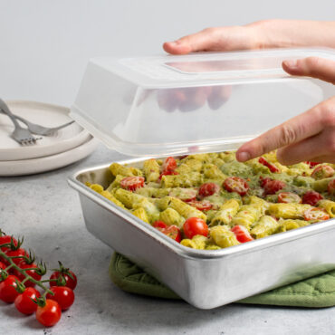 rectangular baking pan with noodle casserole, hands holding lid above pan