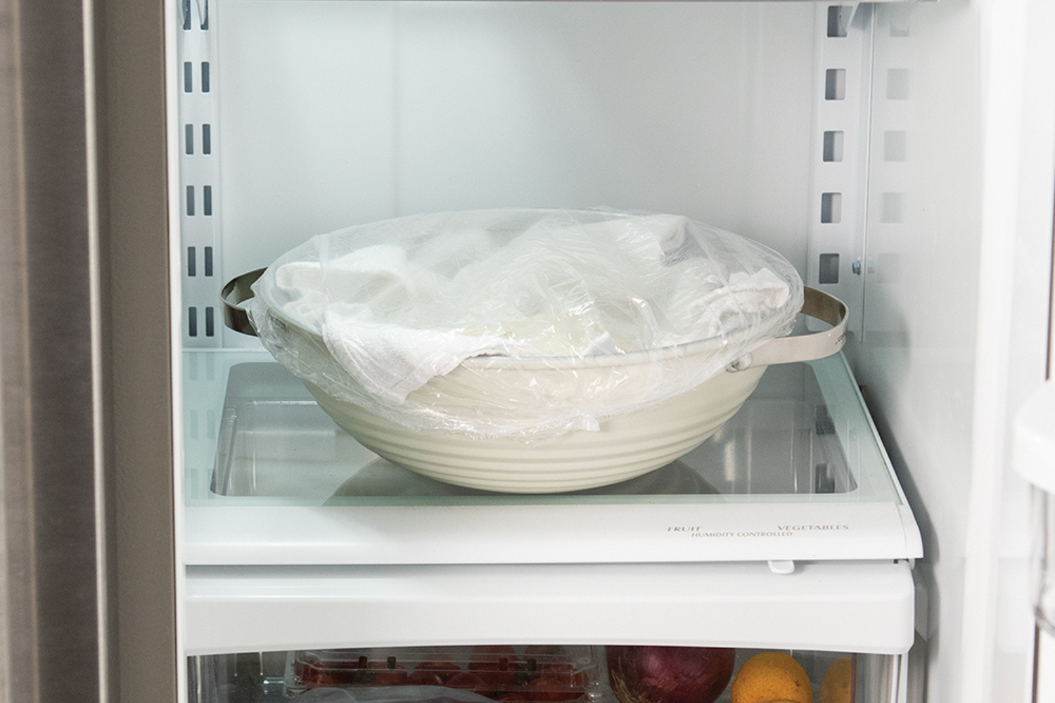 Sourdough bread dough cold proofing in the oven in the sourdough baking lid lined with a cotton proofing towel and covered with a shower cap.