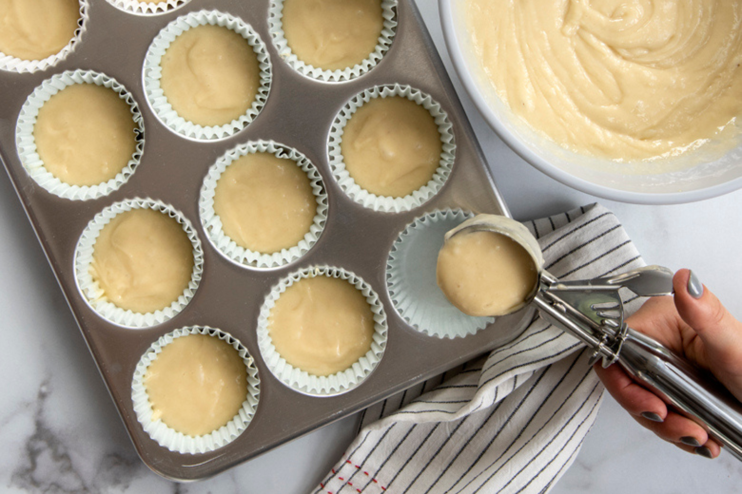 Hand scooping muffin batter into Naturals® 12 Cavity Muffin Pan.