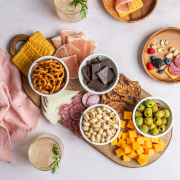 Four mini white bowls on a charcuterie board filled with snacks and cheese