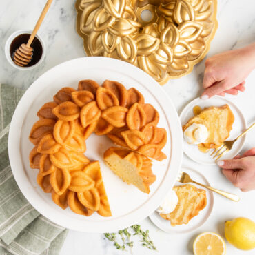 Plain Laurel Wreath Bundt cut into pieces on white cake stand, small pieces with whipped topping on small plates